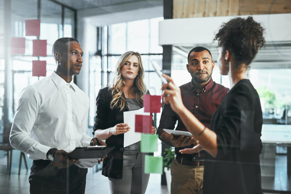 “A diverse group of professionals collaborating in a meeting room around a flipchart with sticky notes discussing strategy”